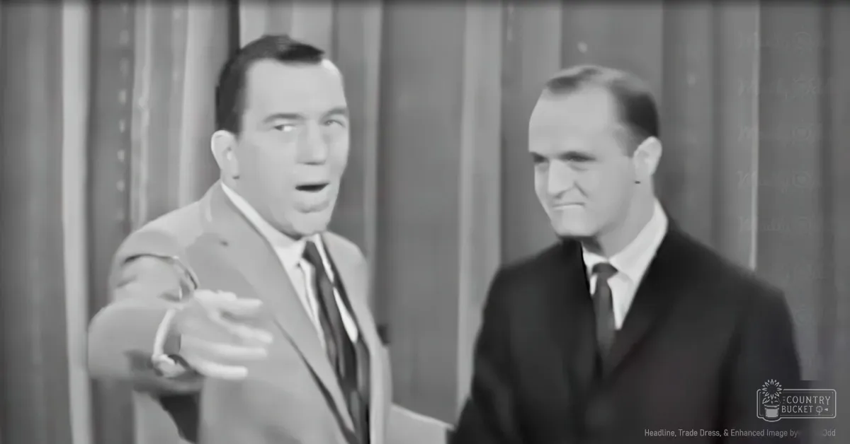 Two men in a studio setting with curtains or paneling as the backdrop; they appear middle-aged and dressed formally, one holding what seems like a hat.