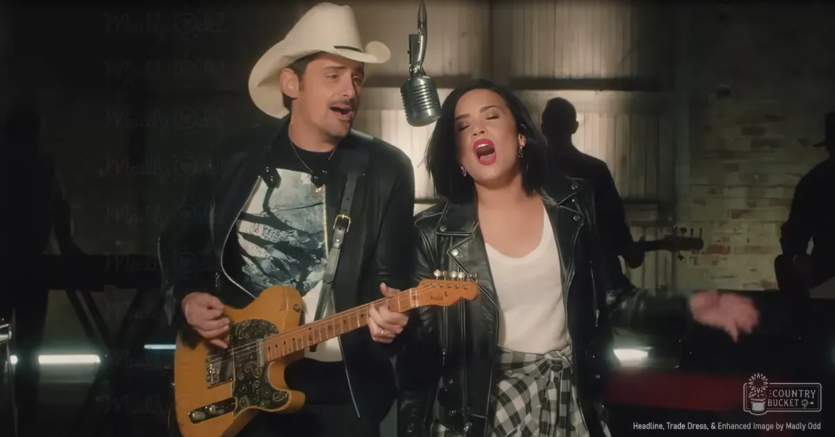 An adult male singer wearing a white cowboy hat and black leather jacket in a recording studio setting with another adult female in a black leather jacket, surrounded by music production elements.