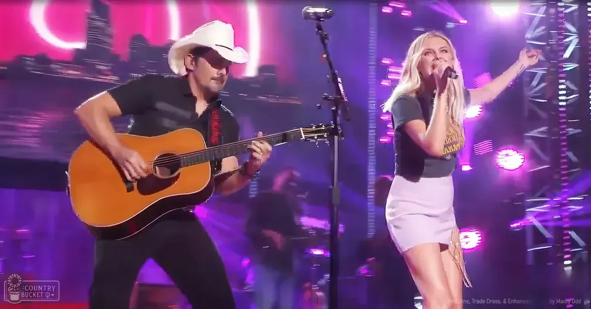 A musical performance scene at an indoor concert venue with vibrant stage lighting; a young adult female wearing a graphic top and skirt, and an adult male in a white cowboy hat performing.