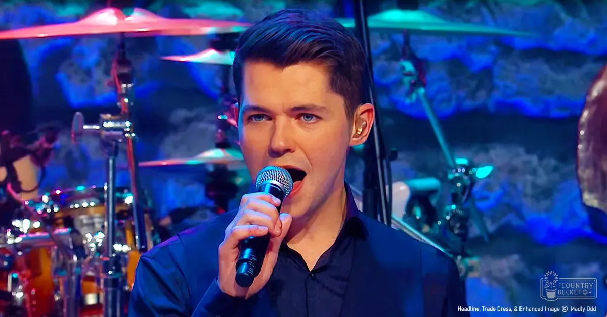 A young adult male in a music studio or stage setting, wearing a dark blue button-up shirt.