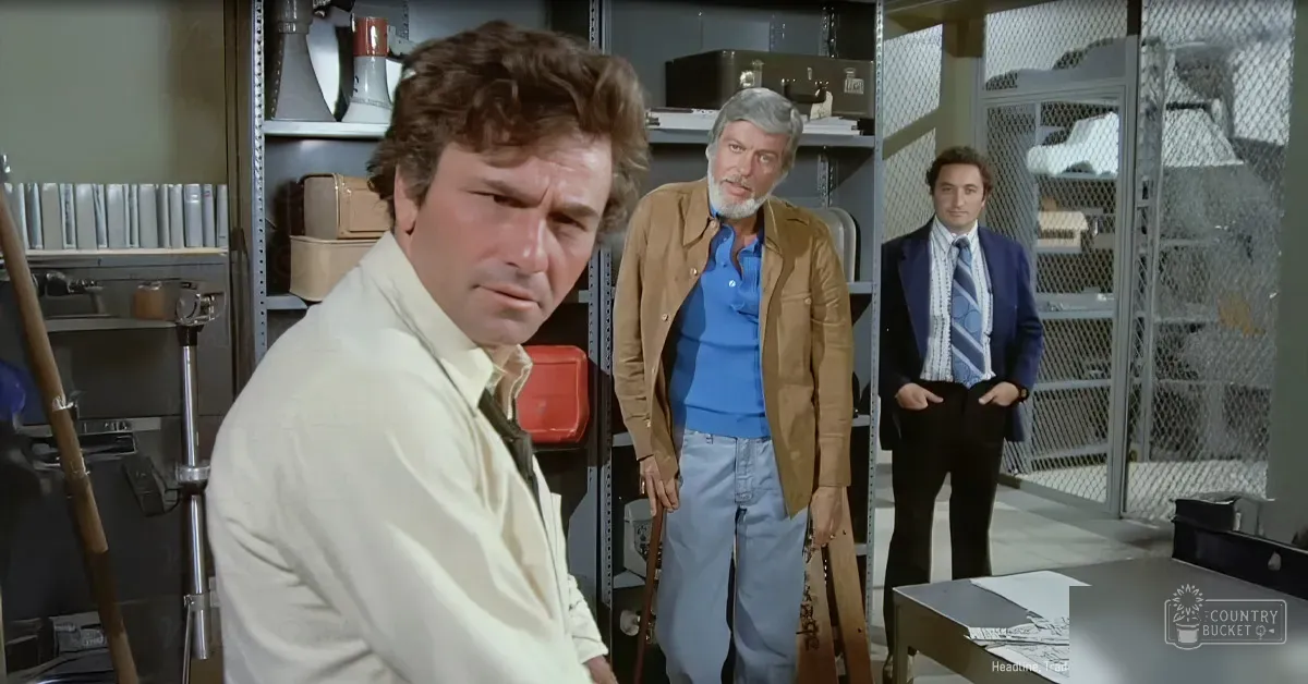 An adult male wearing a light-colored button-up shirt with rolled-up sleeves, standing indoors amidst shelves of files and boxes, suggesting an office or storage room environment.
