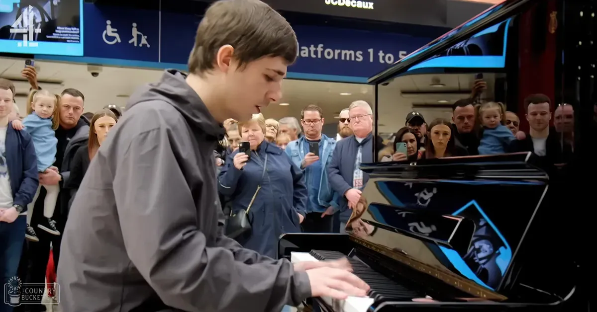 A young adult male plays a glossy black grand piano surrounded by various individuals, including children and adults, at what appears to be an indoor public transportation hub with signage indicating 'Platforms 1 to 5.'