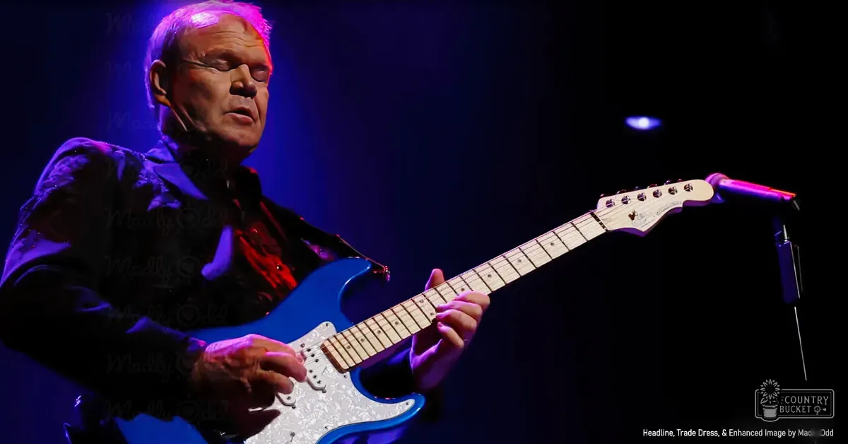 A middle-aged adult male plays guitar indoors under dramatic stage lighting.