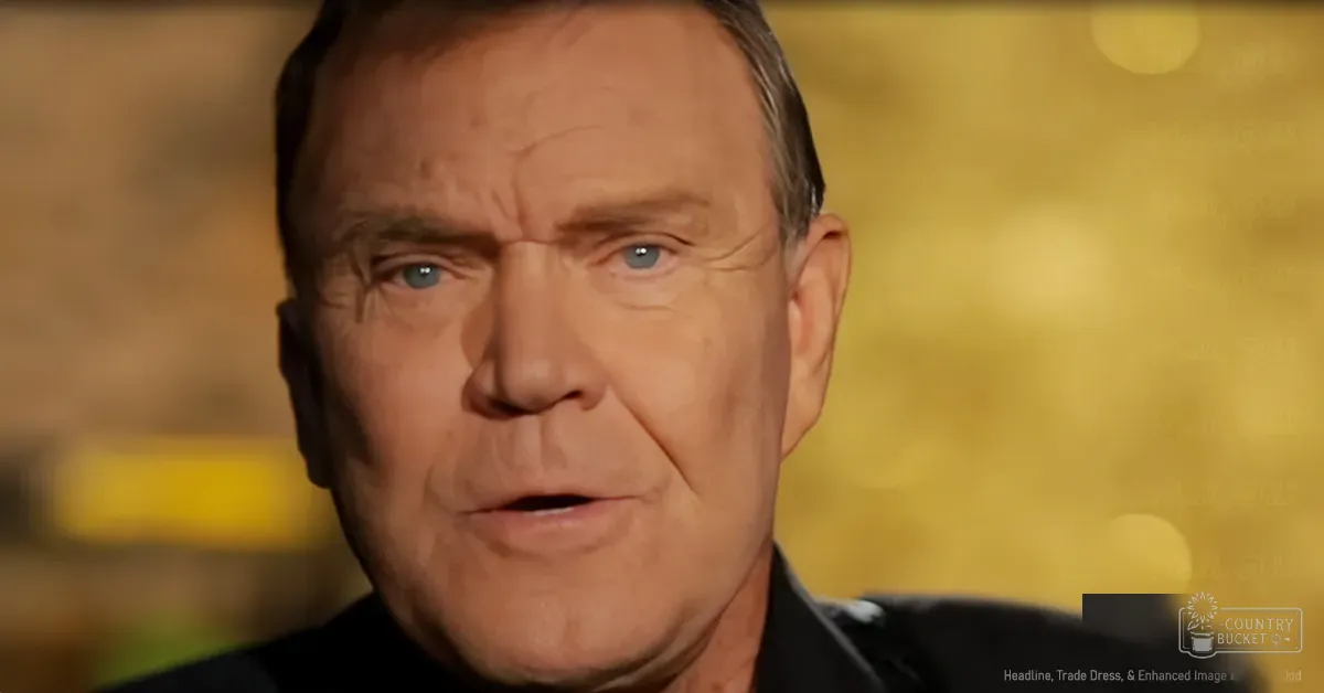 An older adult male wearing a dark, collared shirt in a professional indoor setting with a yellowish background.