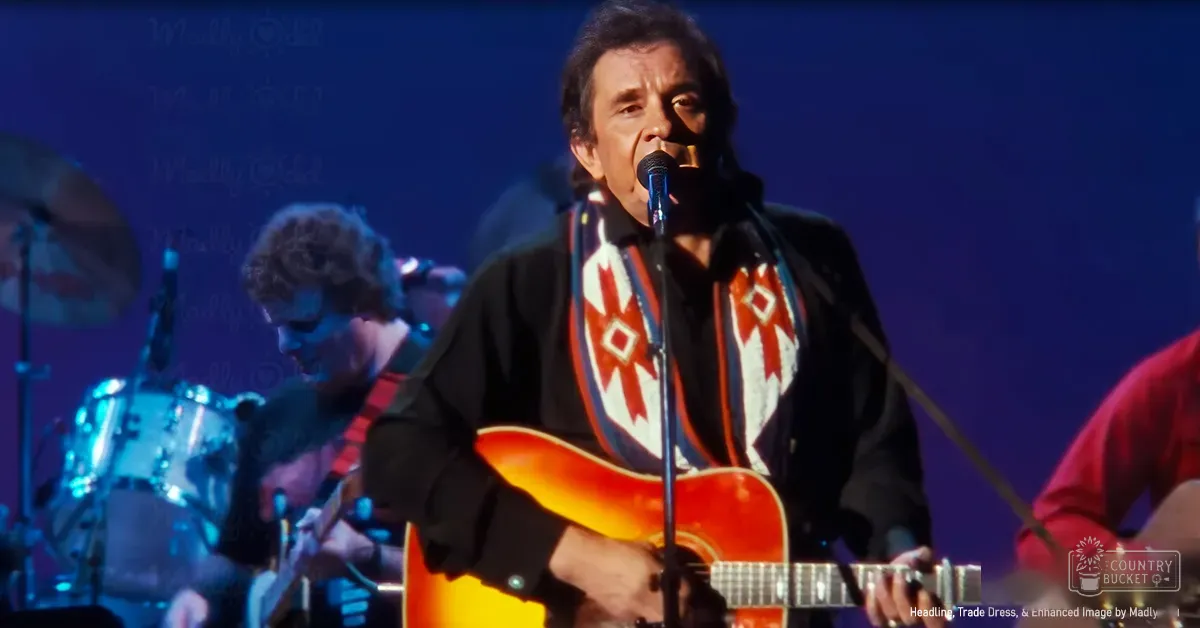 A middle-aged male singer wearing a black jacket with a red and white patterned scarf around his neck, holding a yellow guitar on stage in an indoor concert setting.