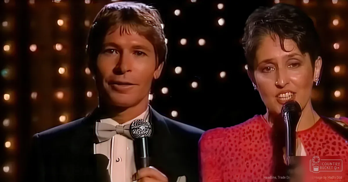 A musical performance scene with a young adult male singer wearing a black tuxedo and a gray bow tie, and an adult female performer in a red dotted dress on stage under warm bokeh lighting.