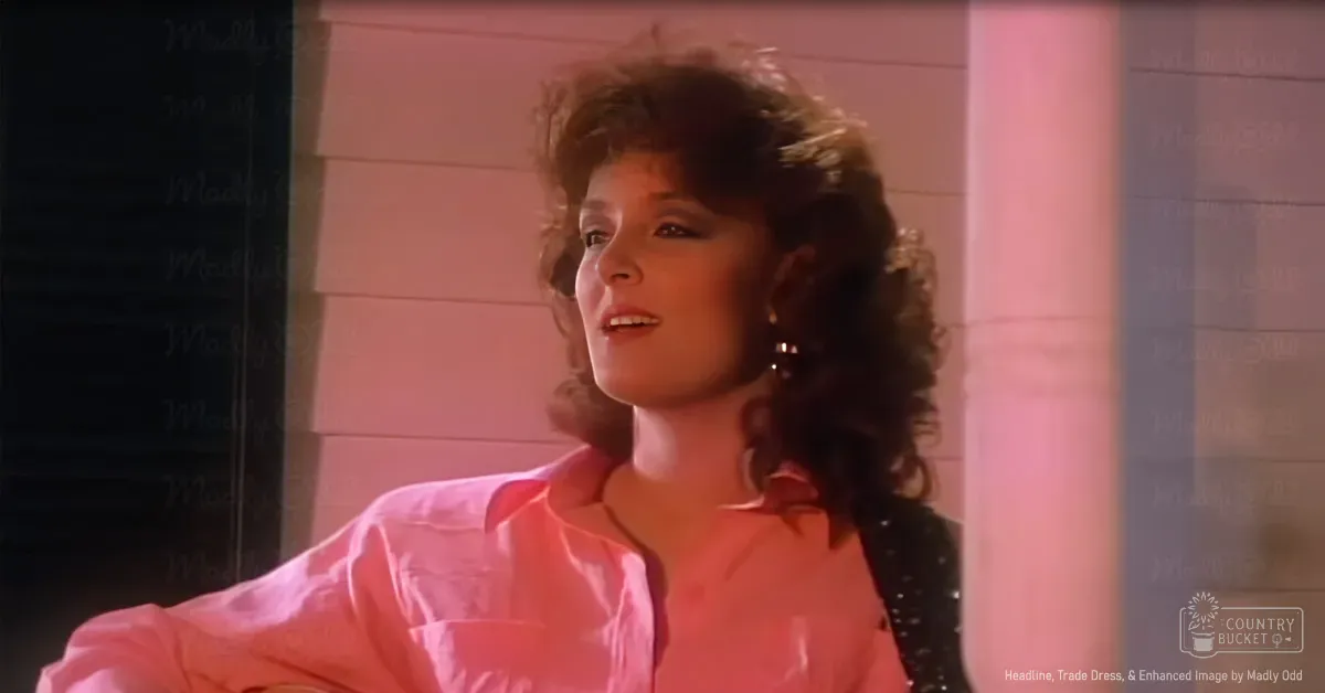 Young adult female in a casual indoor setting wearing a pink button-up shirt with relaxed fit and large hoop earrings, surrounded by natural daylight and pink-toned background elements.