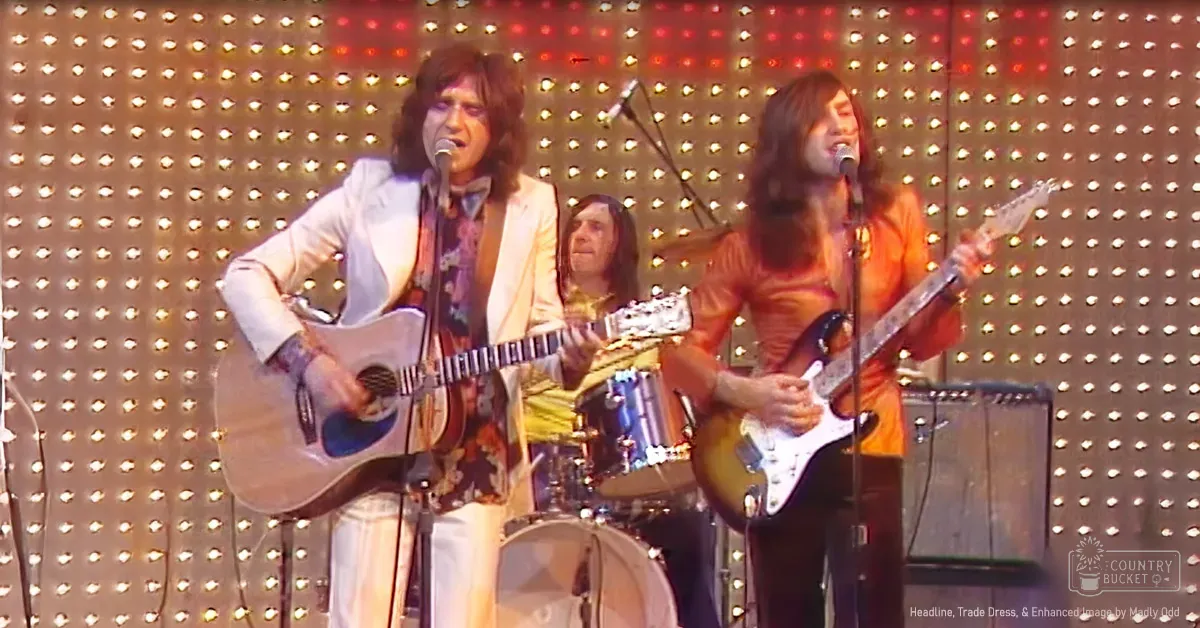 An indoor musical performance scene with microphones, amplifiers, a drum set, and performers in patterned shirts and jackets under artificial lighting at night.