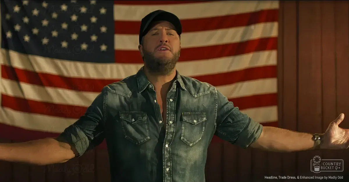An adult male wearing a dark denim shirt with rolled-up sleeves stands indoors against an American flag, suggesting a rustic or patriotic theme. The setting is illuminated by natural light, giving the scene a warm tone.