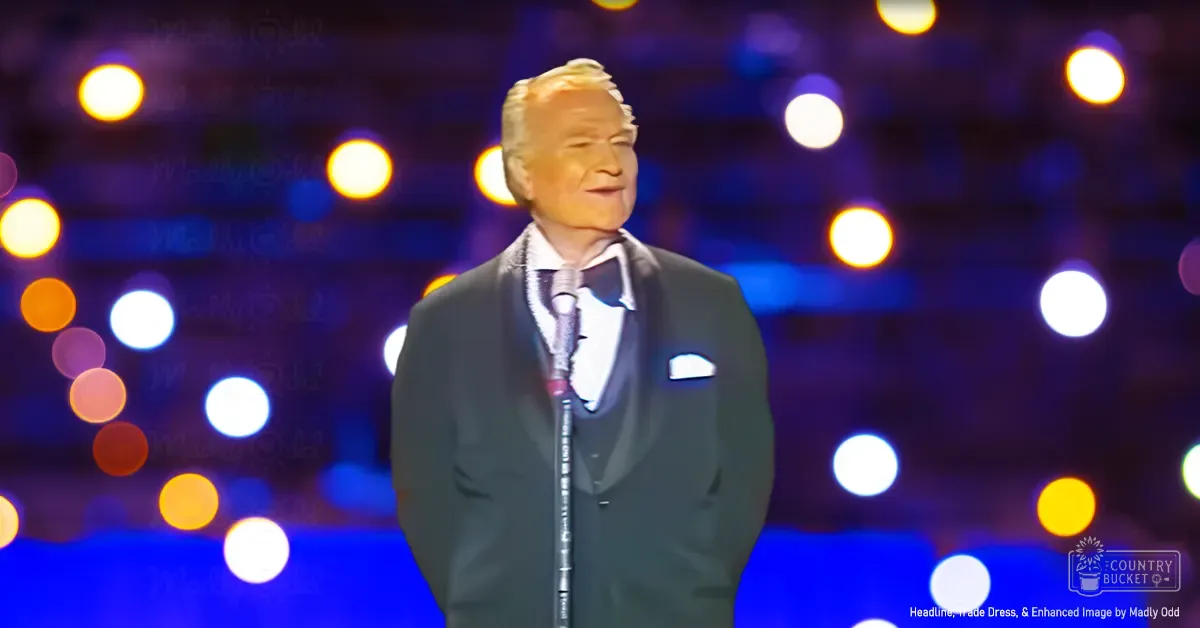 A male performer in a dark suit with a white pocket square and bow tie at an indoor stage performance setting with vibrant bokeh lighting effects.