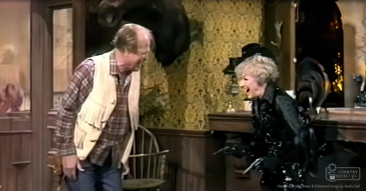 Middle-aged male in a plaid shirt interacting with an older adult woman wearing a black leather jacket and hat, indoors in a home setting with warm lighting.