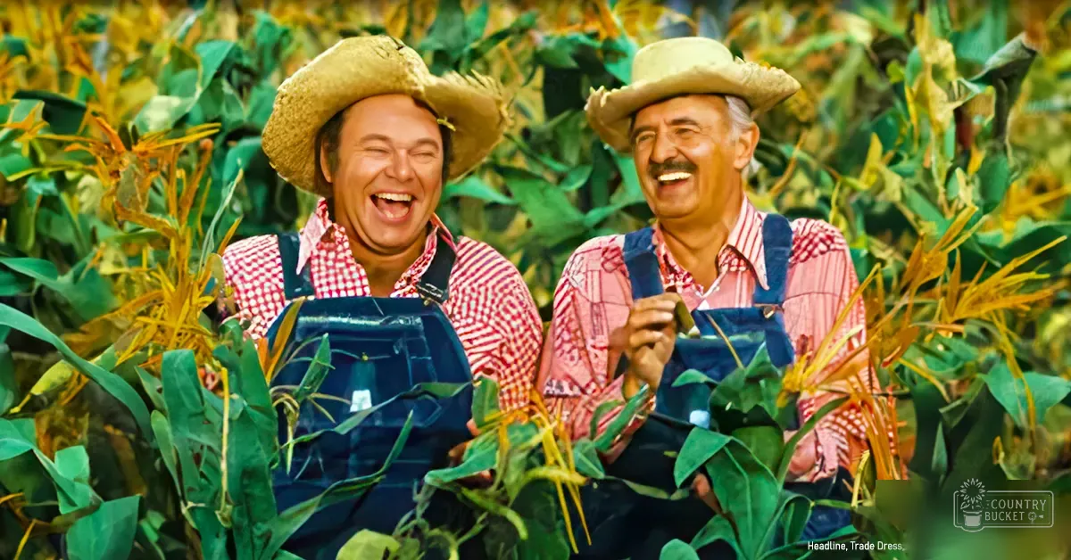 Two adult males wearing red and white checkered cotton overalls with collared shirts underneath, straw hats, standing in a lush green cornfield under bright daylight during summer.