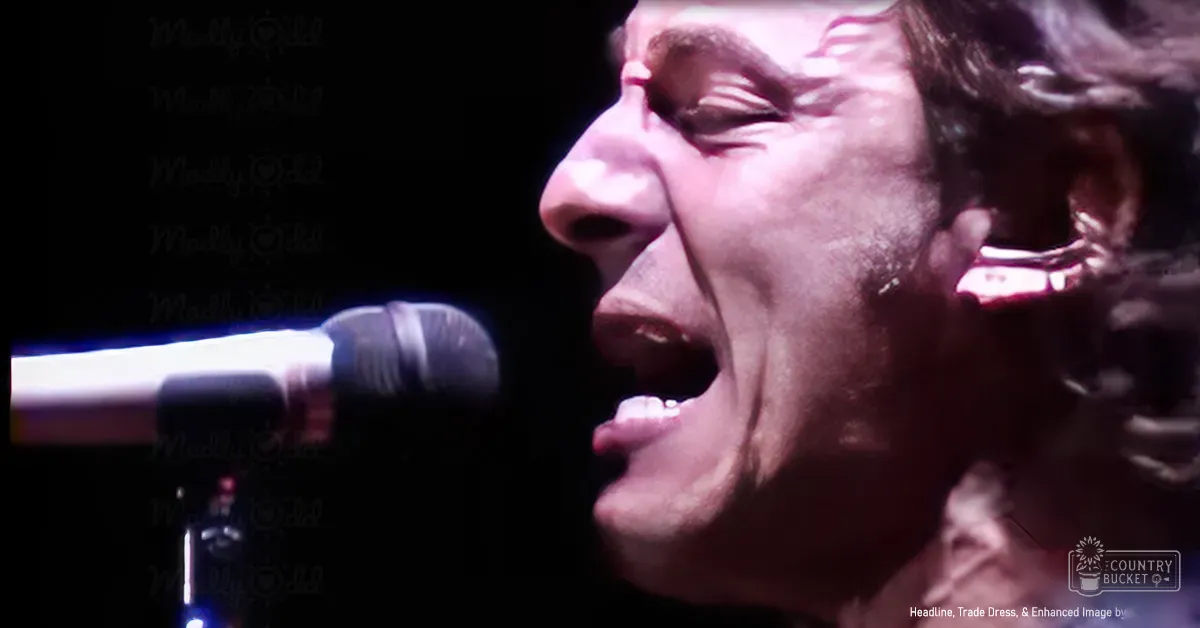 An adult male performer singing into a microphone at an indoor concert venue under artificial lighting.
