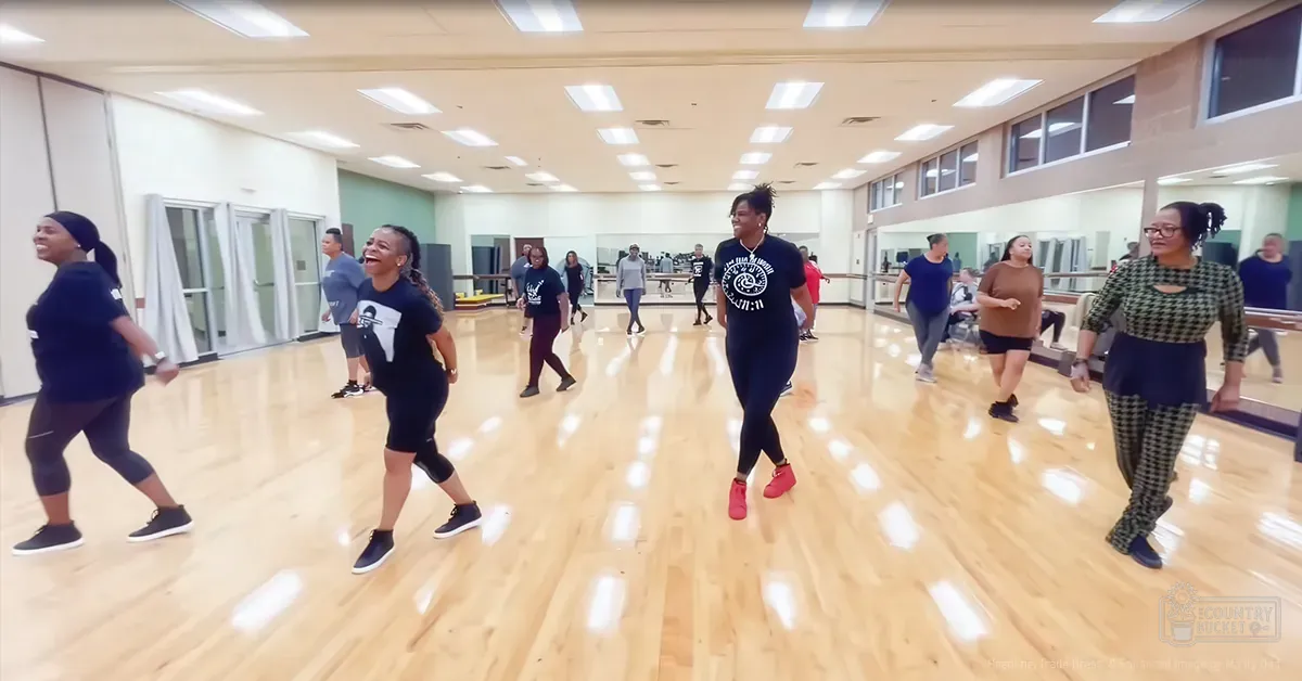 A dance class in progress at a studio with adults wearing various styles of athletic wear under natural light.