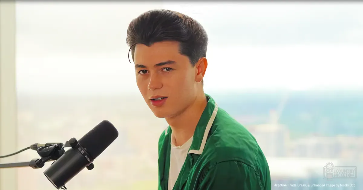 Young adult male wearing a green jacket with white trim, holding a black microphone against an urban backdrop.