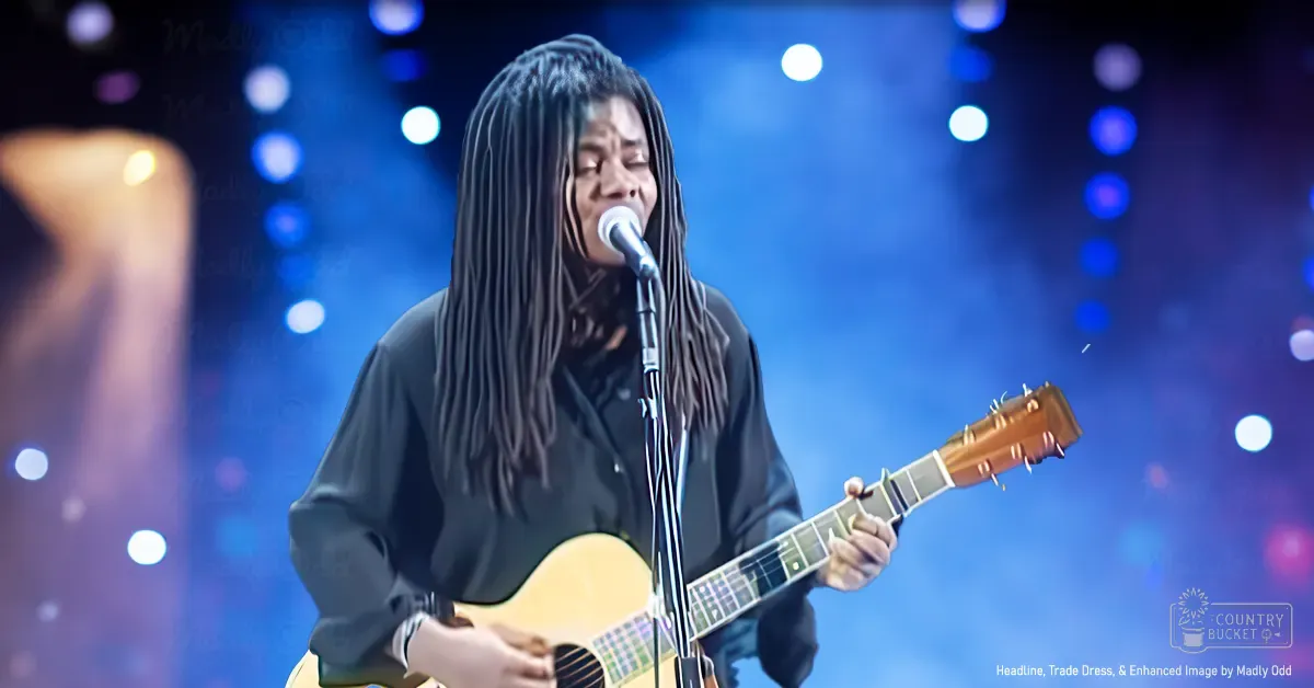 A female adult wearing a black, relaxed-fit long-sleeve shirt with soft cotton blend material performs live on an indoor concert stage under blue and white bokeh lighting.