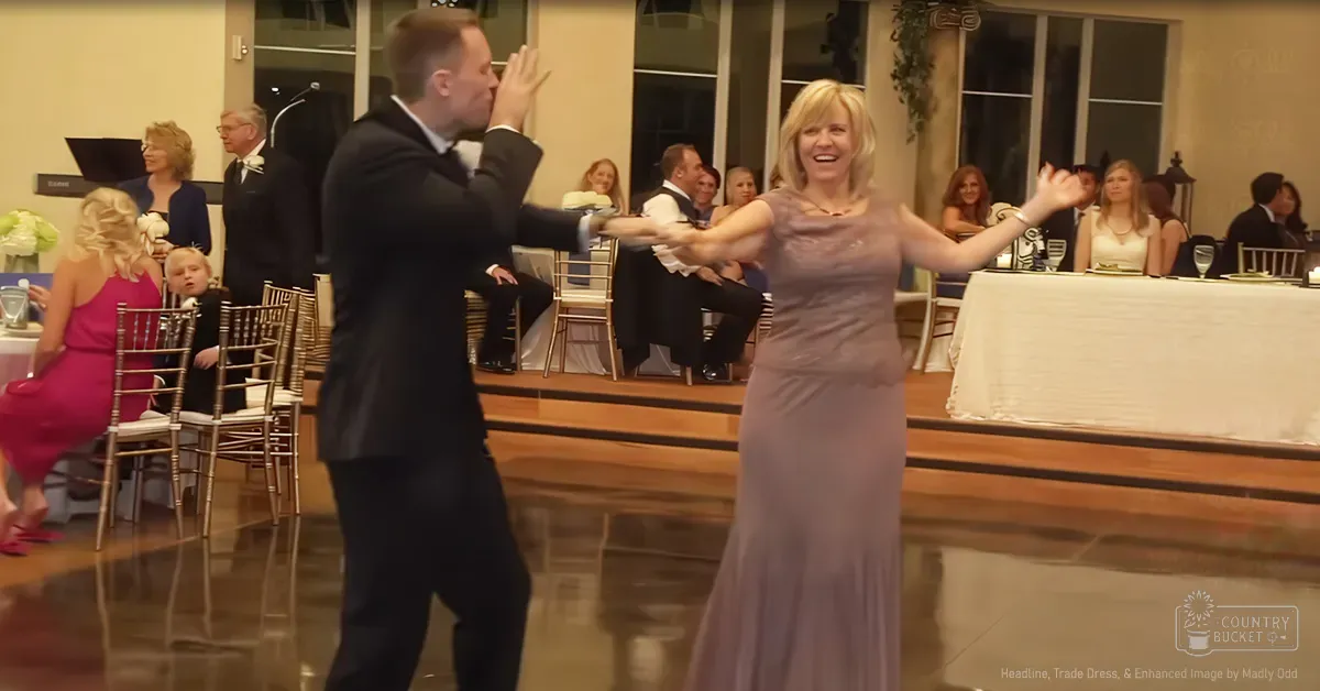 A couple dancing at an indoor wedding reception with tables covered in white tablecloths and floral arrangements.
