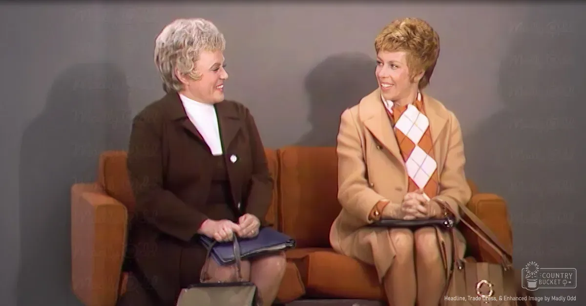 Two women in a studio setting, one wearing a dark brown blazer with beige high-heeled shoes, holding a blue clutch; the other in a light tan coat and plaid scarf, holding a brown handbag. Professional lighting suggests an indoor interview or talk show setup.