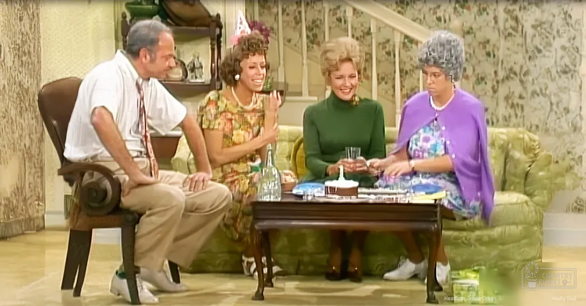 Adults gathered indoors in a living room setting with floral wallpaper and mid-century decor.