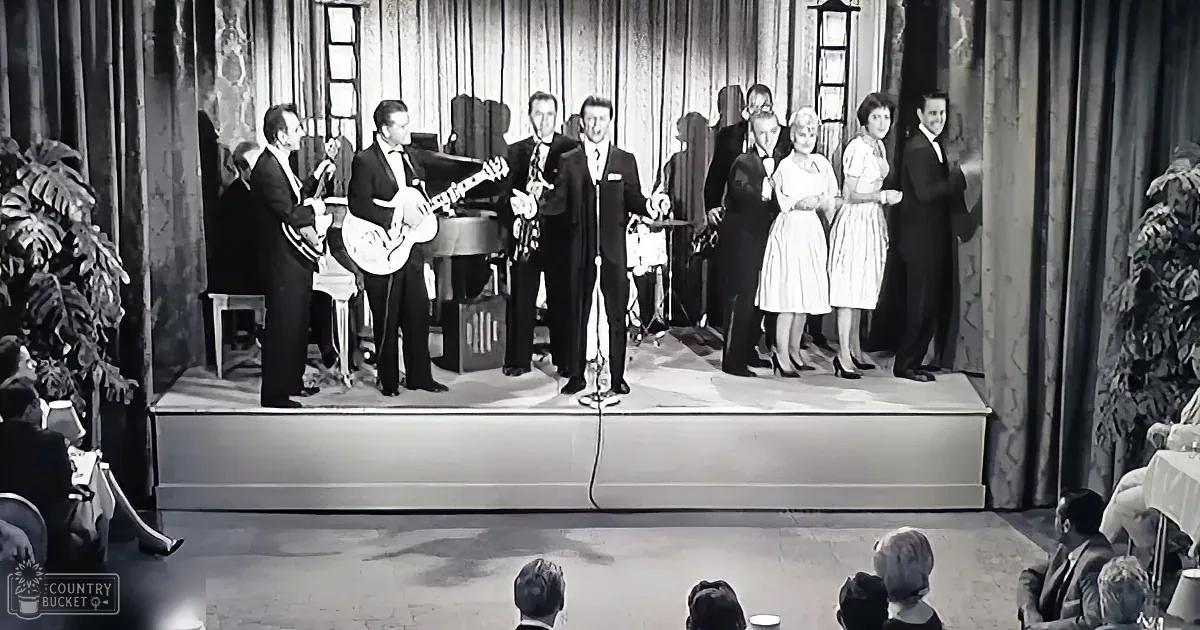 A band and singers perform on stage, with musicians playing instruments and a microphone in the foreground.