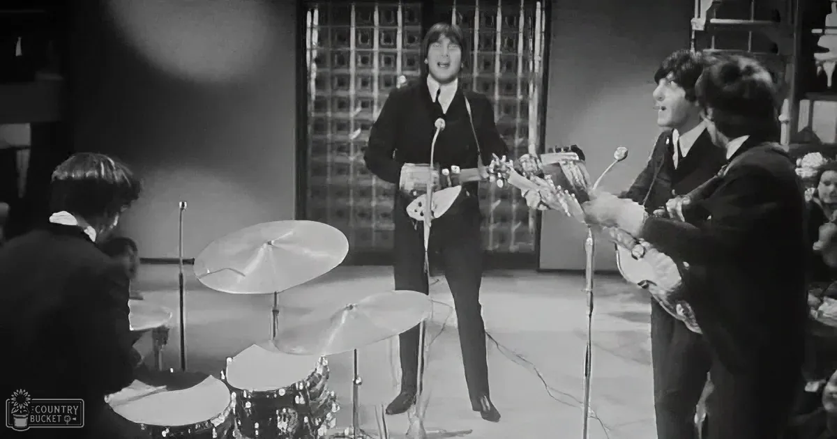 The Beatles perform on stage, John Lennon sings, Paul McCartney plays bass, Ringo Starr drums, George Harrison plays guitar.