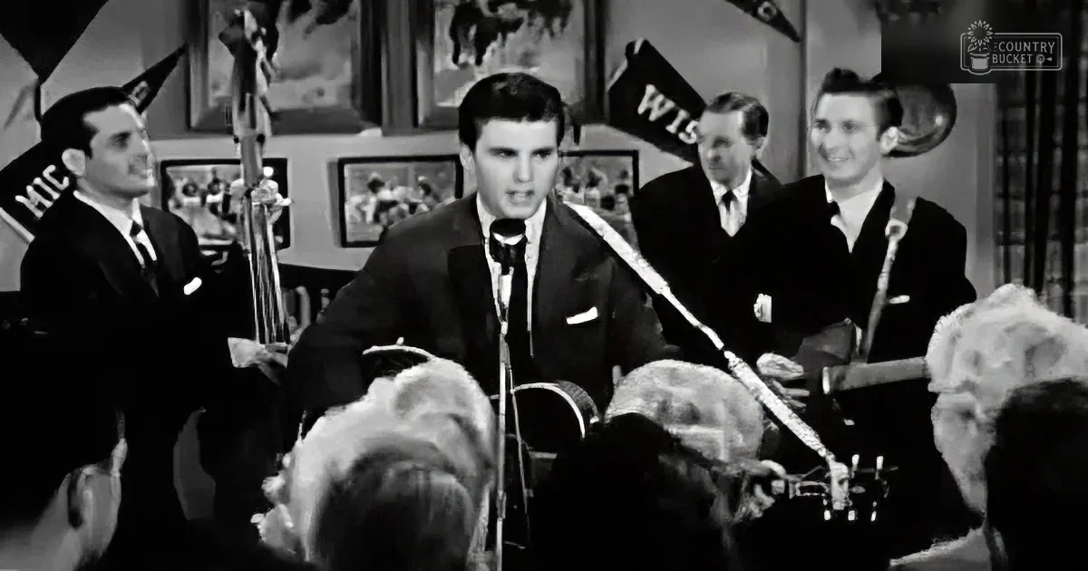 Elvis Presley performs on stage with a band, surrounded by a crowd and vintage decor.