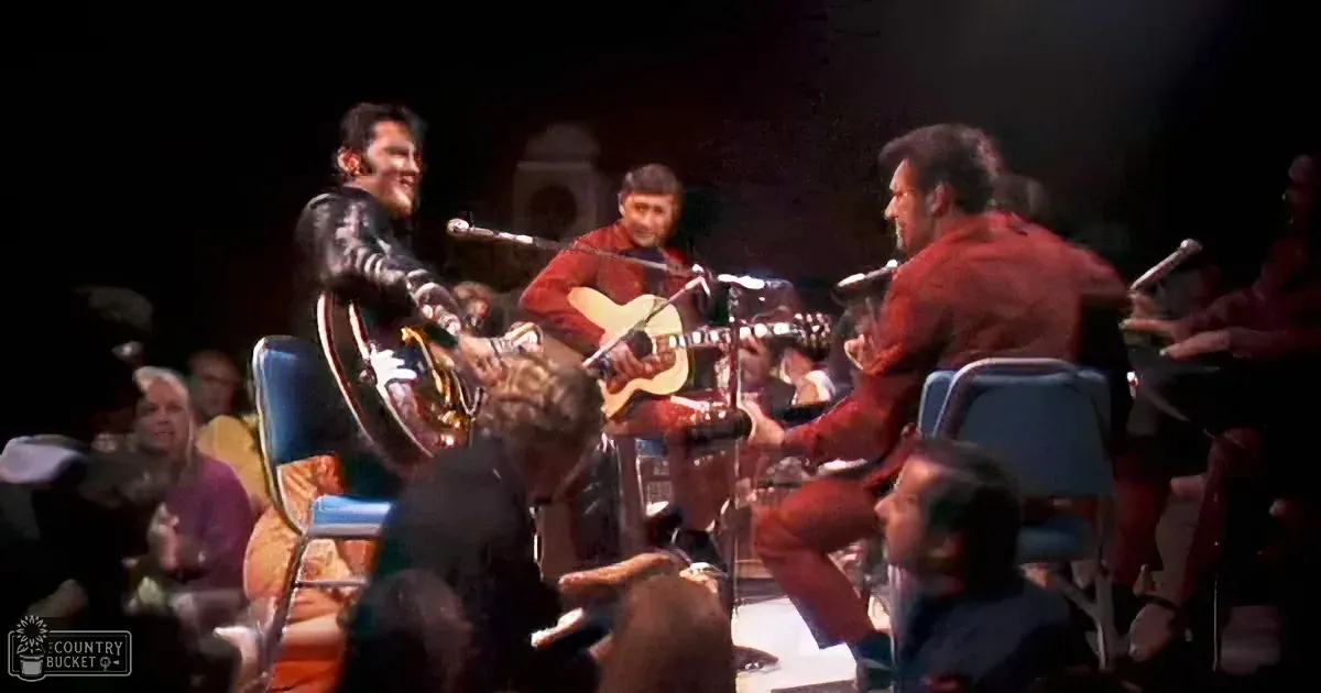 Elvis Presley plays guitar on stage with a band and audience in the background.