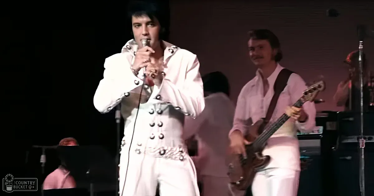 Elvis Presley in a white suit sings into a microphone on stage.