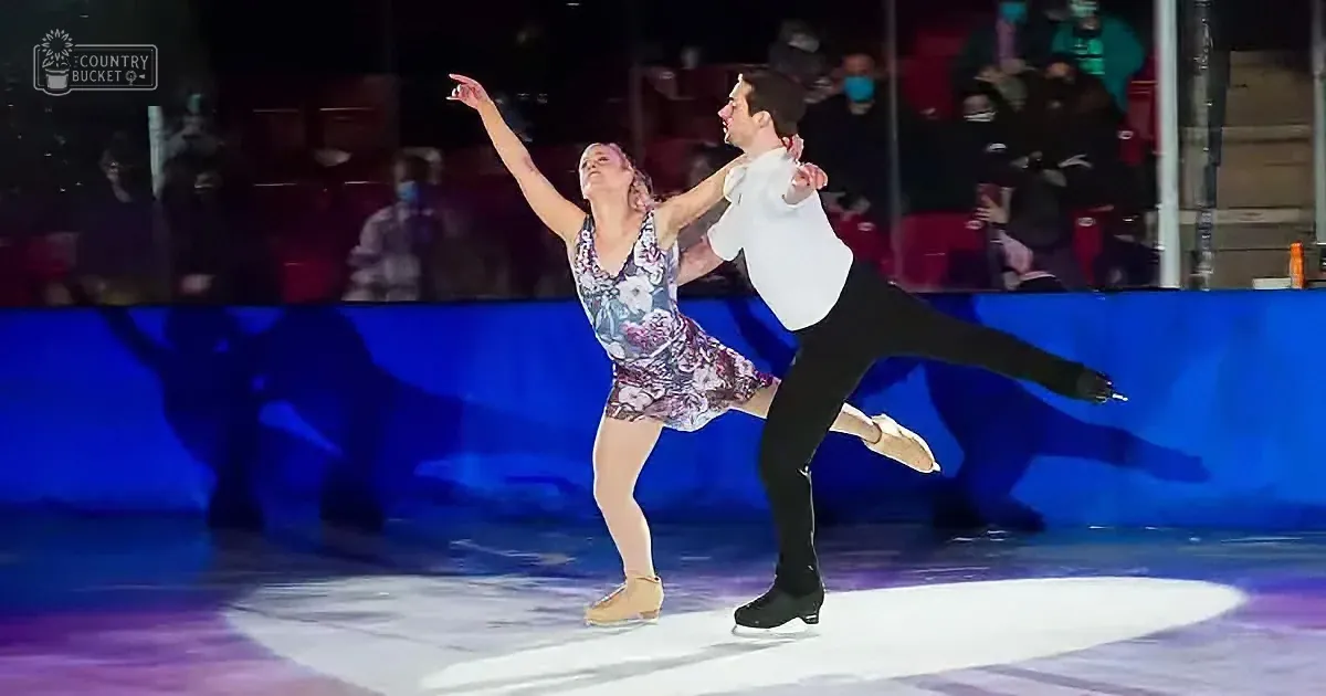 A figure skating couple performs a lift on ice, with the woman in a floral dress and the man in a white shirt and black...