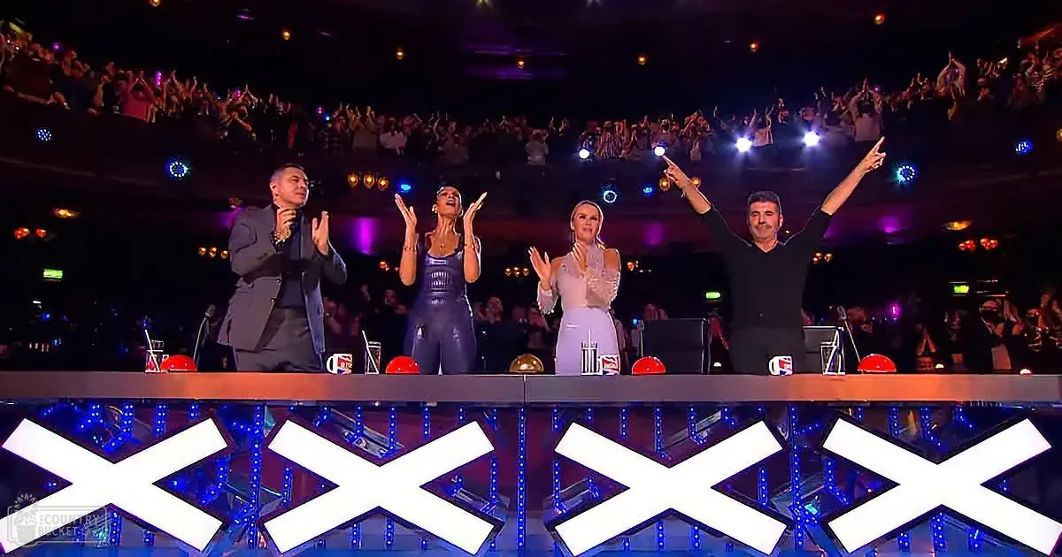 Four judges on stage with arms raised, audience cheering in the background.