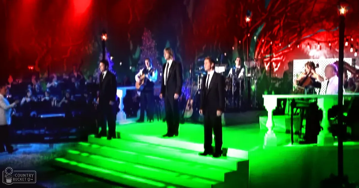 An adult male singer performing at an indoor concert venue with theatrical lighting and stage decorations.