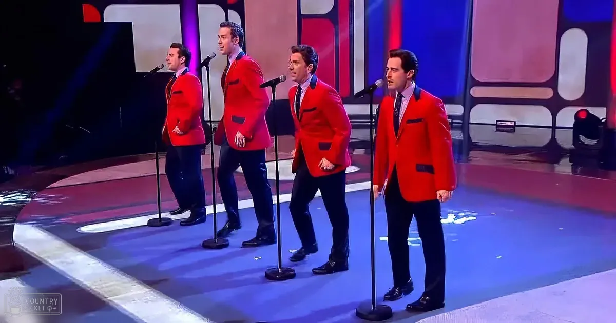 Four men in red suits sing on stage with microphones, wearing black pants and ties.