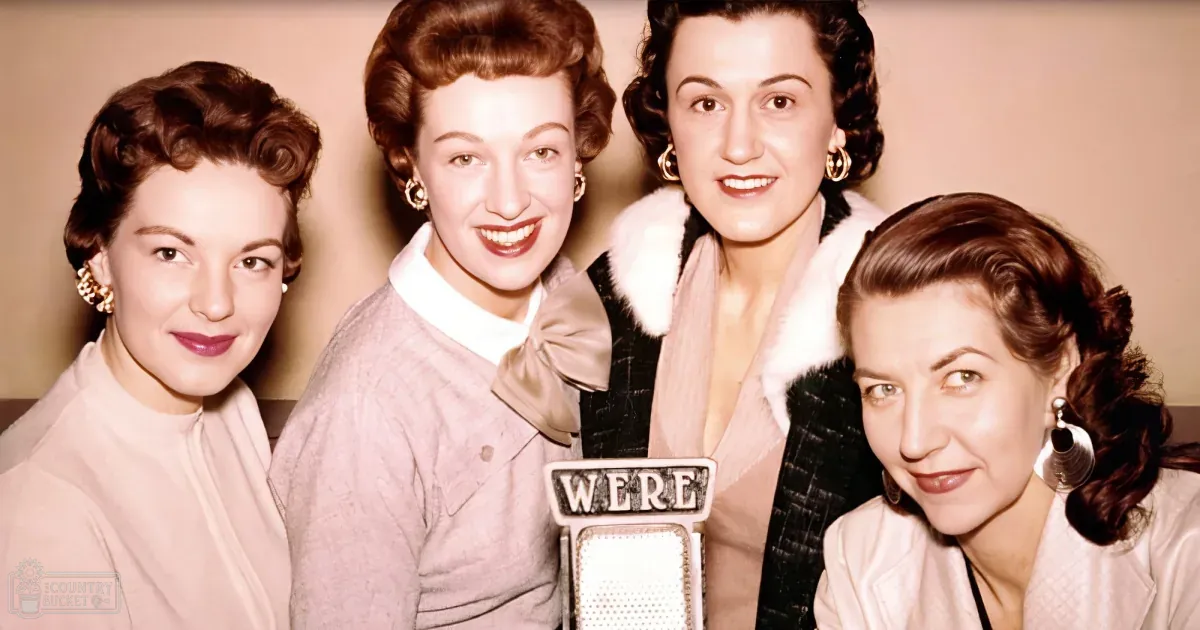 Four women in vintage attire pose together, smiling, with one holding a microphone.