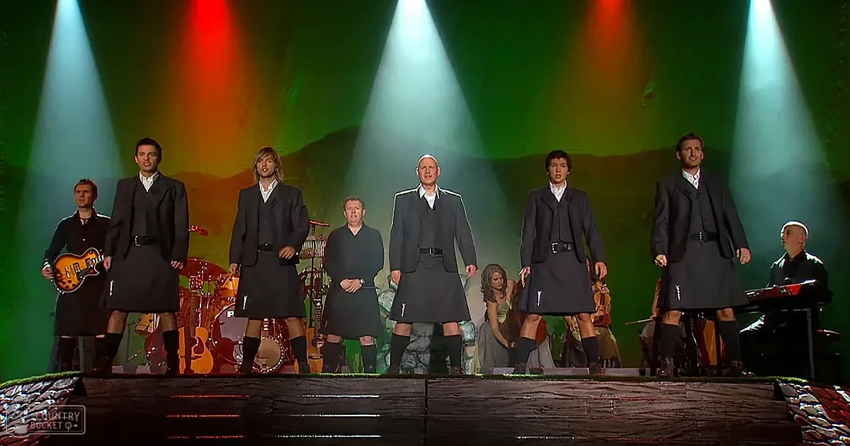 A group of men in kilts performs on stage under colorful spotlights.