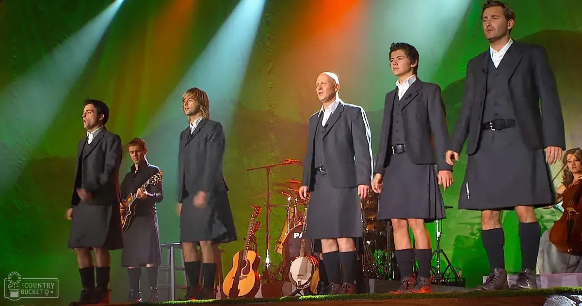 A group of men in kilts and suits perform on stage with musical instruments.