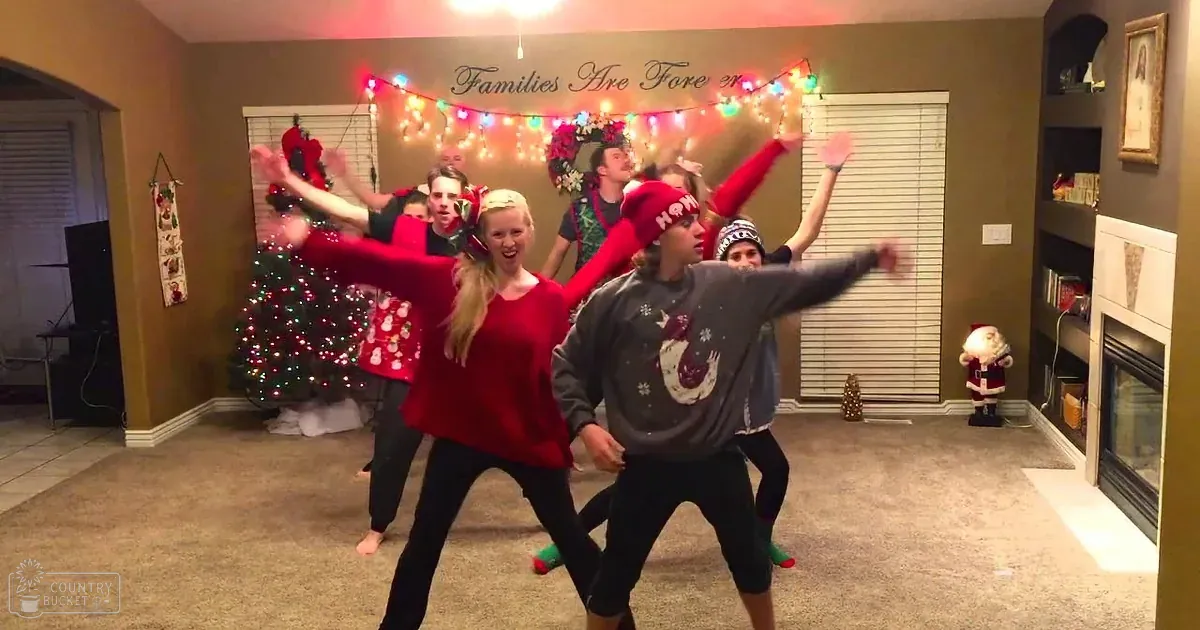 Group of young adults in festive indoor setting, likely during Christmas. Grand piano, decorated Christmas tree with lights and ornaments, cuckoo clock, small train set visible.