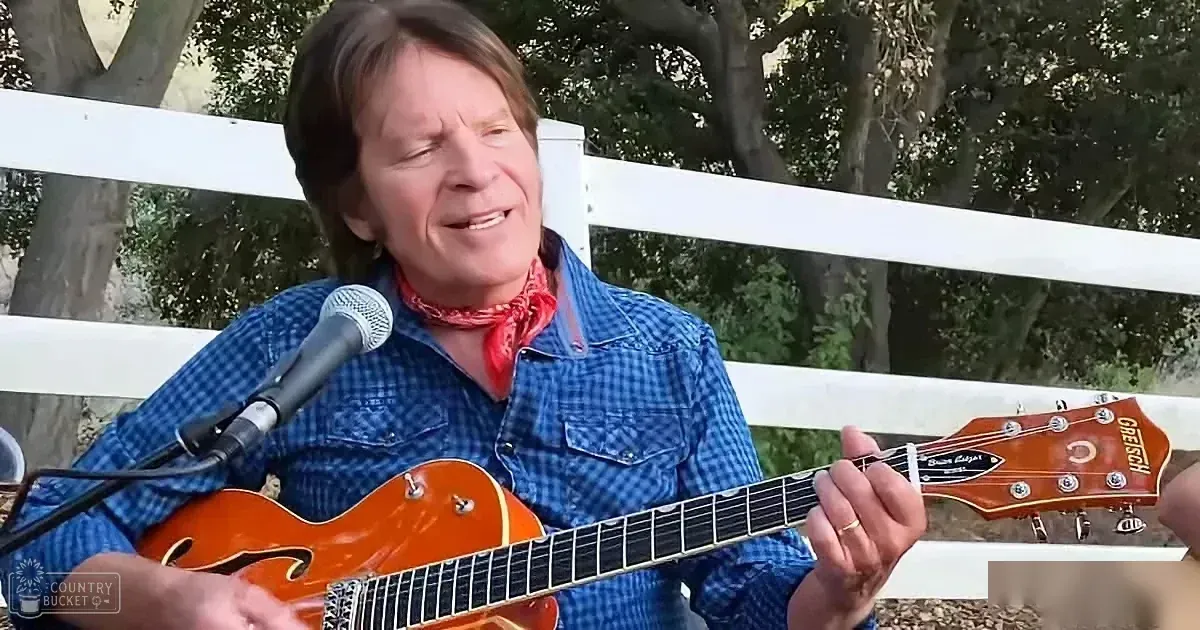 A man in a blue plaid shirt plays a Gretsch guitar, singing into a microphone outdoors.