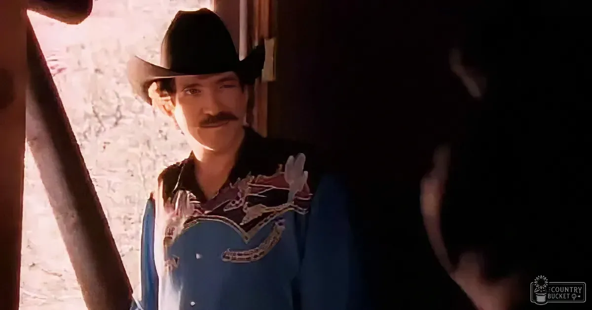 A man in a cowboy hat and blue shirt stands in a doorway, looking to the side.