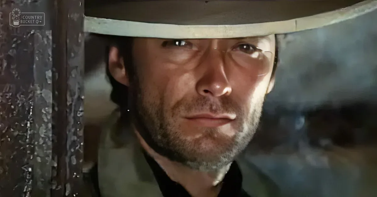 A man in a cowboy hat looks intense, framed by a metal structure, with a rugged expression.