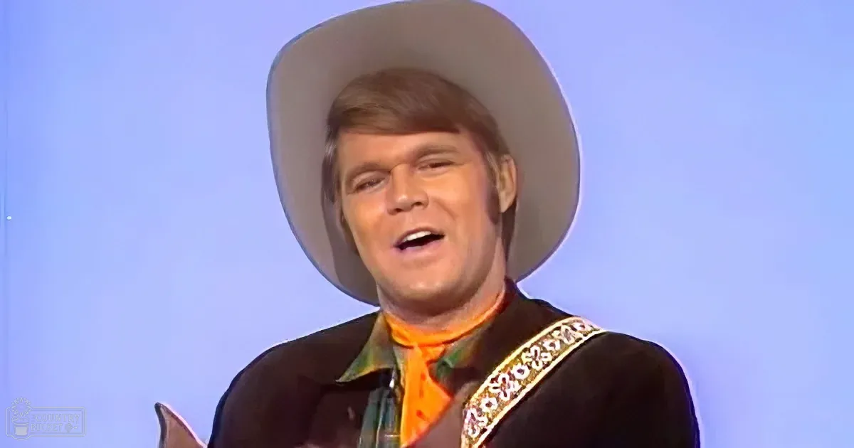 A man in a cowboy hat and western attire is singing, with a bright orange scarf and a blue background.