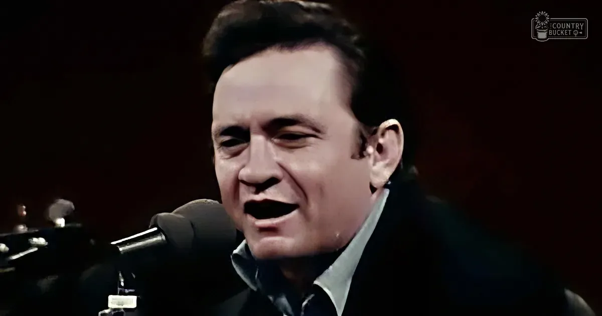 A man in a dark suit sings passionately into a microphone, with a guitar partially visible.