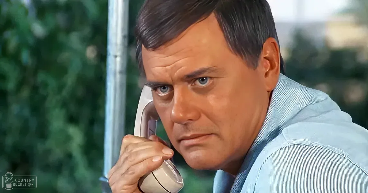 A man in a light blue shirt holds a white telephone receiver to his ear, looking concerned.