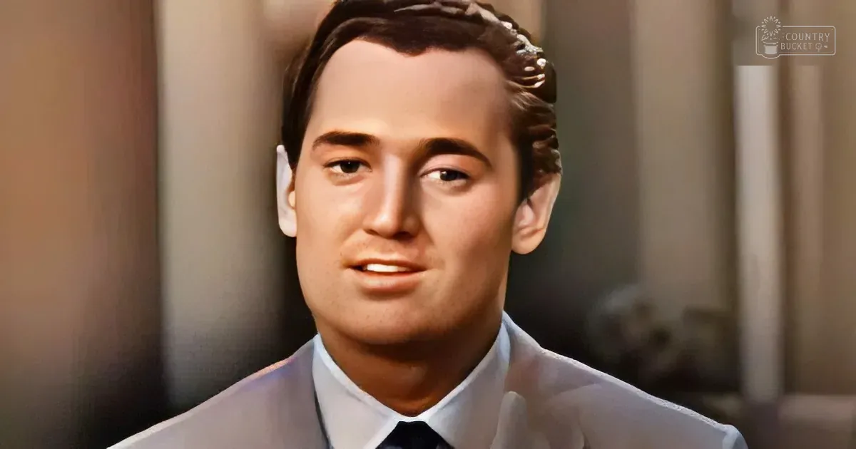 A man in a light suit and tie, looking slightly to the side, with a blurred background.