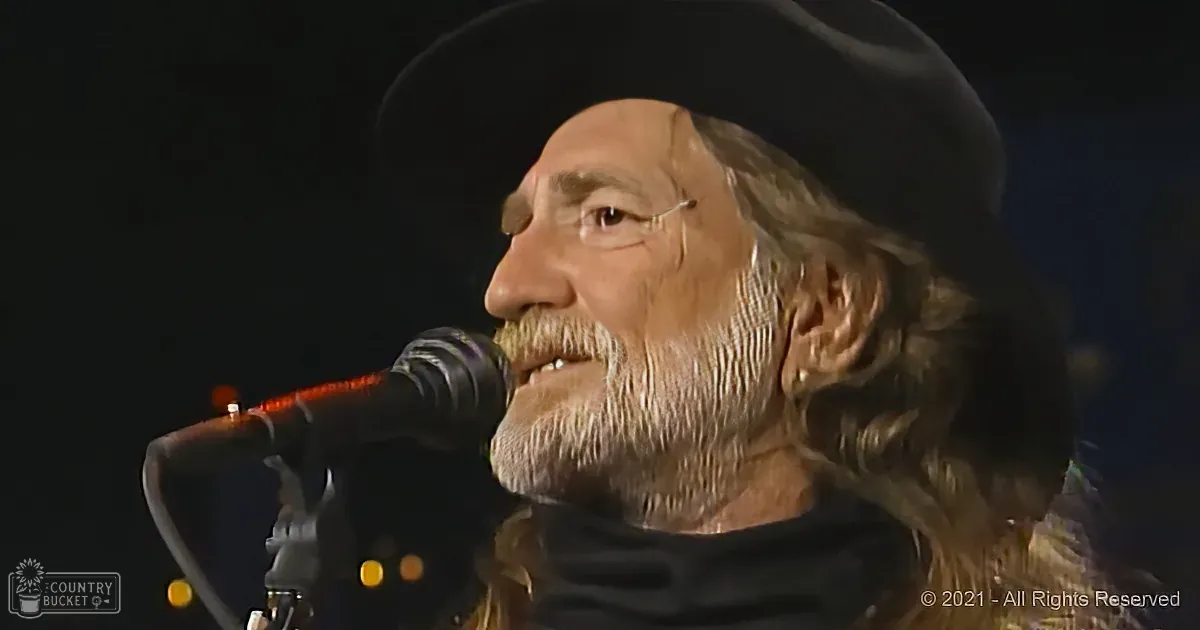 A man with long hair and a beard sings into a microphone, wearing a dark hat.