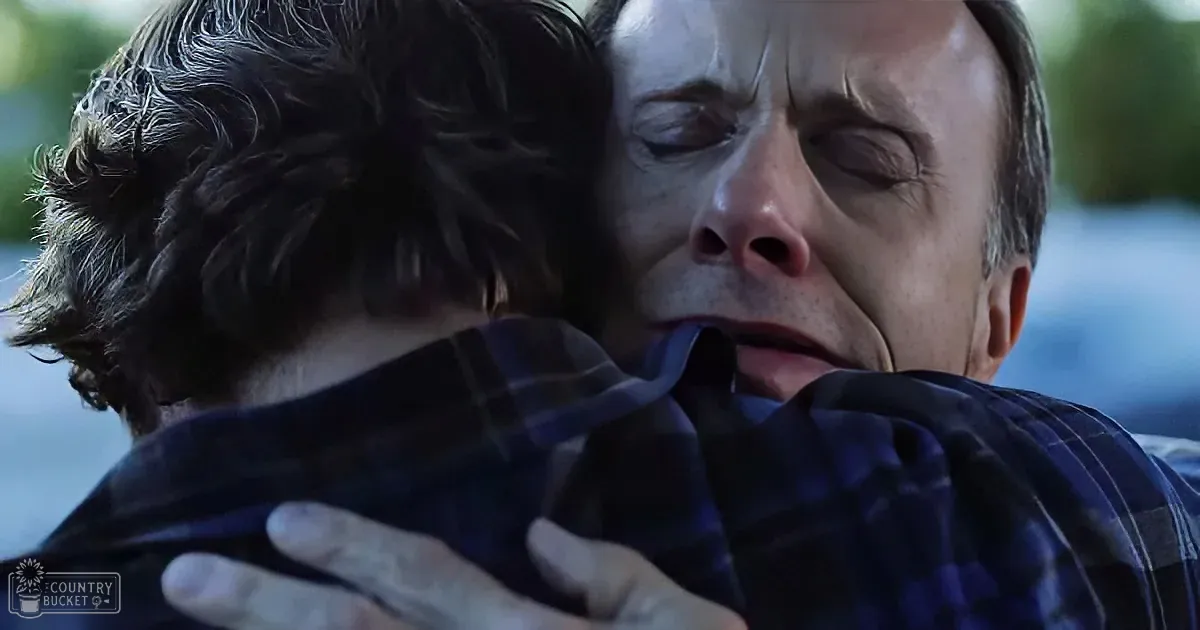A man in a plaid shirt is hugging another person, both appearing emotional and distressed.