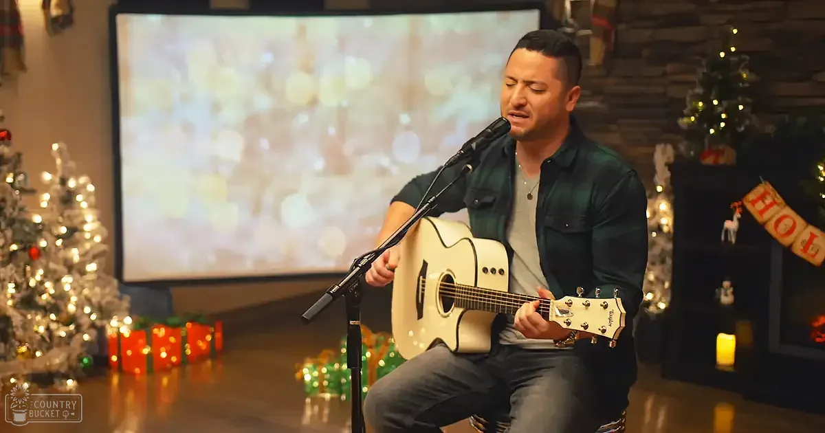 A man plays guitar and sings in front of a Christmas-themed backdrop with lights and decorations.