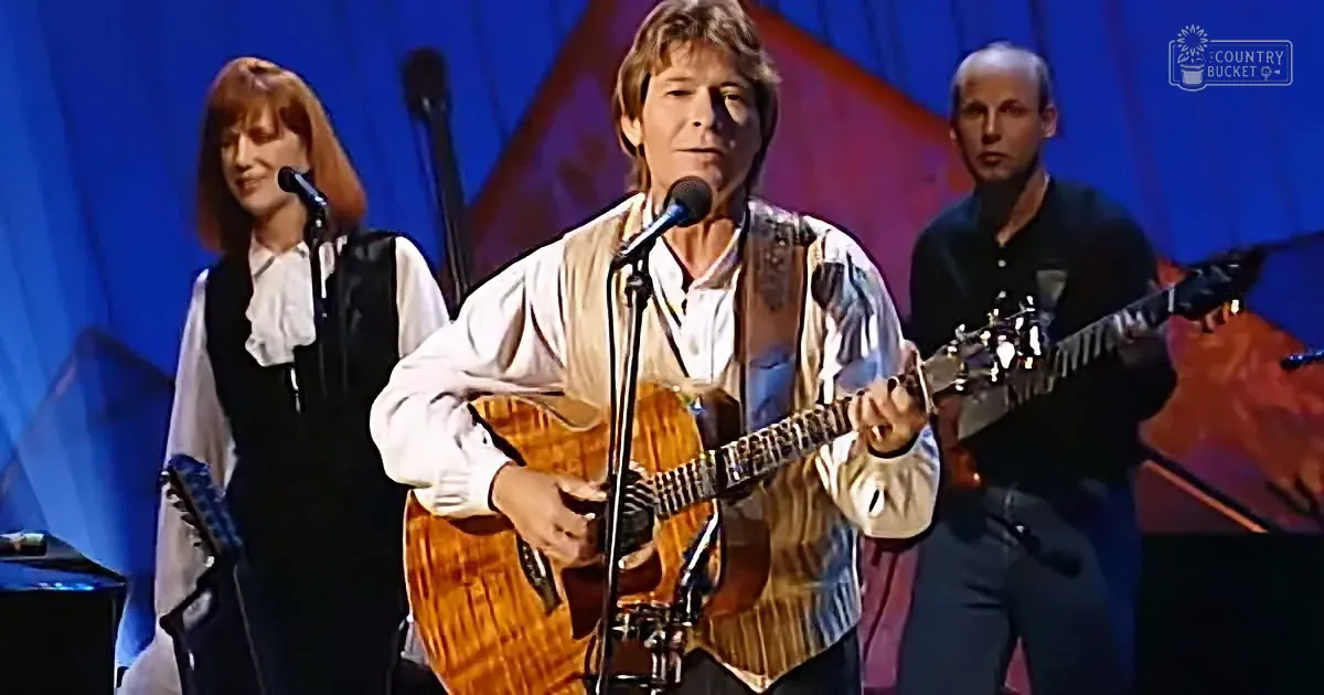 A man plays guitar on stage, singing into a microphone, with two other musicians behind him.