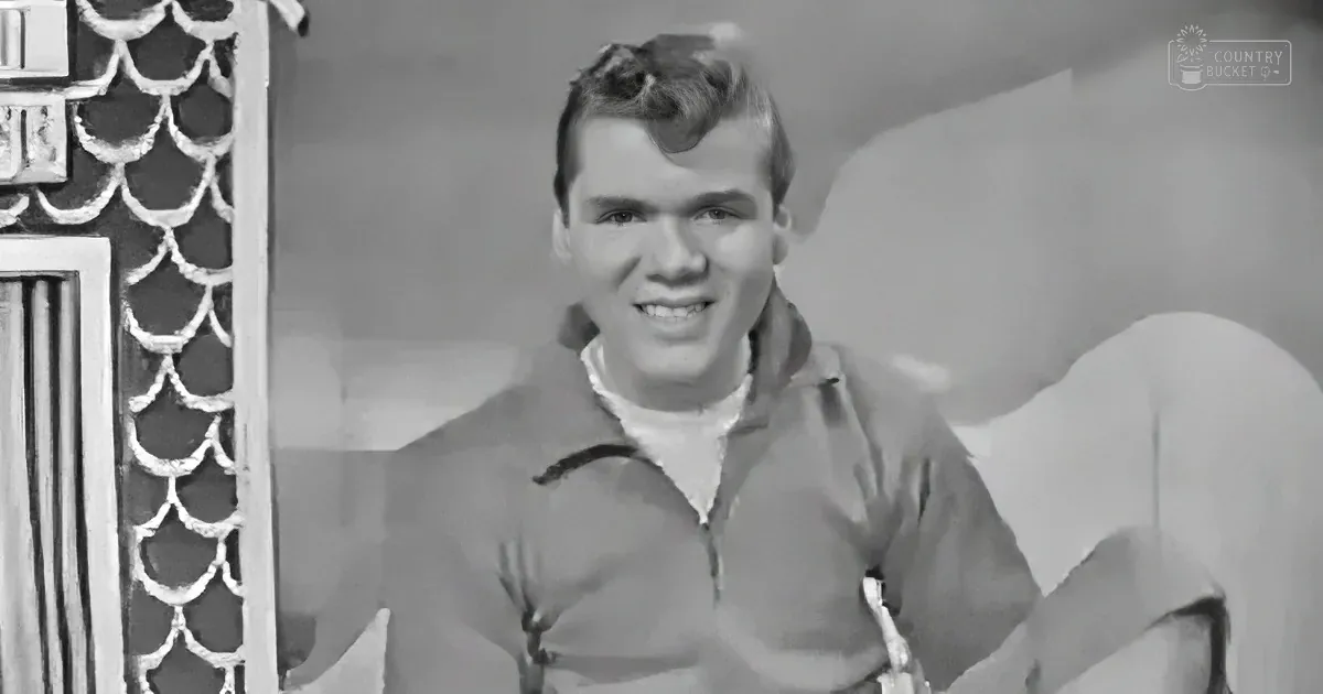 A man in a polo shirt smiles, sitting on a couch with a decorative wall behind him.