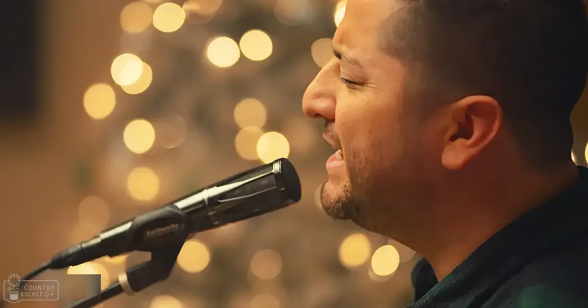 A man sings into a microphone with a blurred background of warm lights.