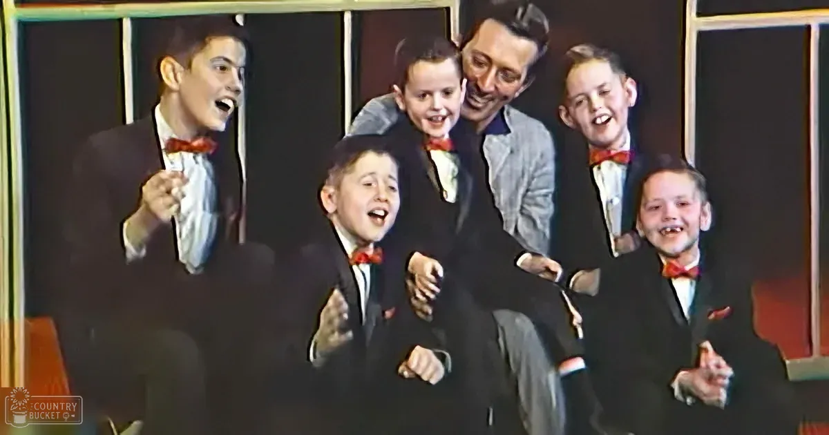 A man in a suit and bow tie is surrounded by five young boys in suits and bow ties, all smiling and laughing.